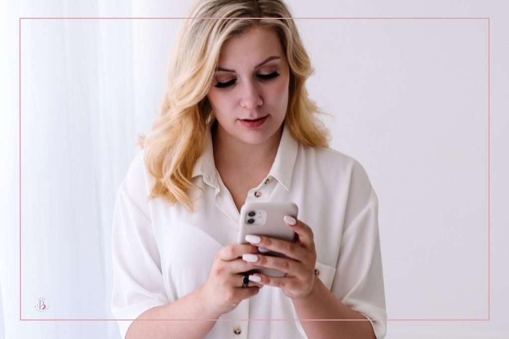 blonde woman wearing a white blouse looking at her cellphone