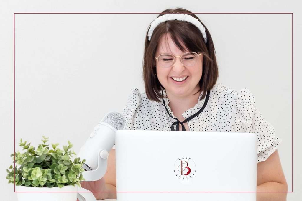 female podcaster with dark hair sitting in front of her laptop. Microphone and green potted plant are on the left.