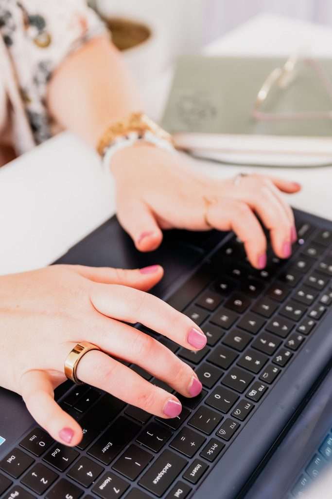 woman with pink nail polish typing on keyboard