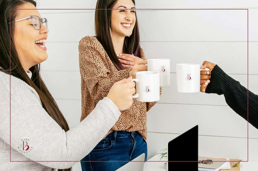 three women cheering each other on by toasting with their coffee cups that have "Barb Wagstaff" logo.