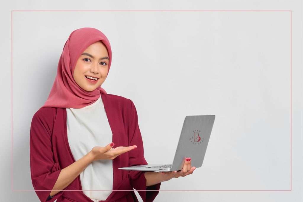 A woman wearing a pink hijab looking happily at her computer screen seeing her online business stand out above the competition.